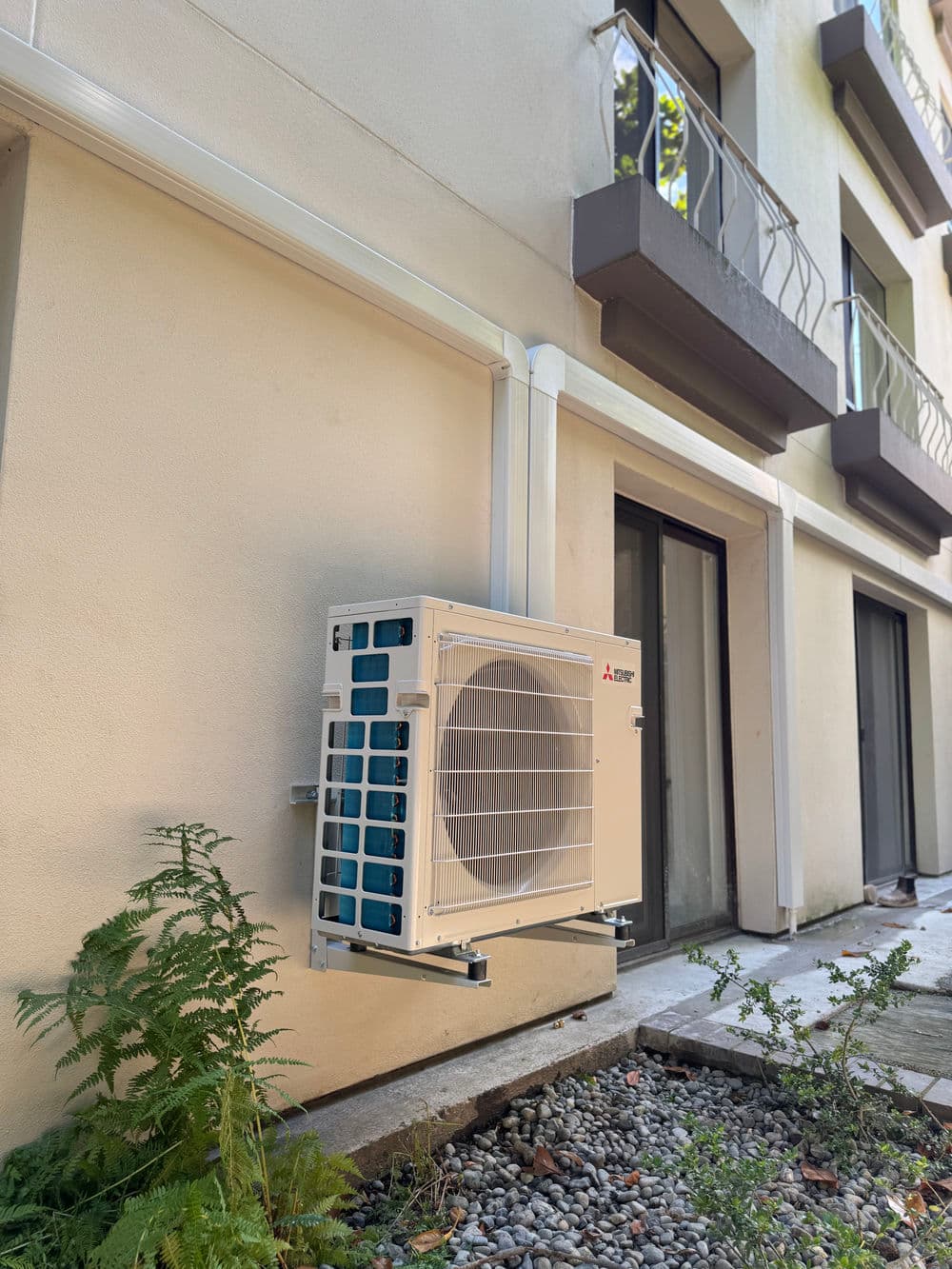 Mitsubishi air conditioning unit mounted on a building exterior with greenery below.