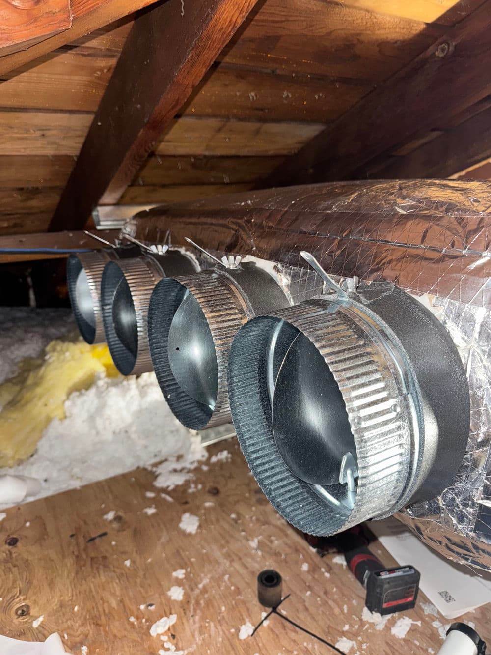 Ventilation ducts with adjustable dampers installed in an attic space.
