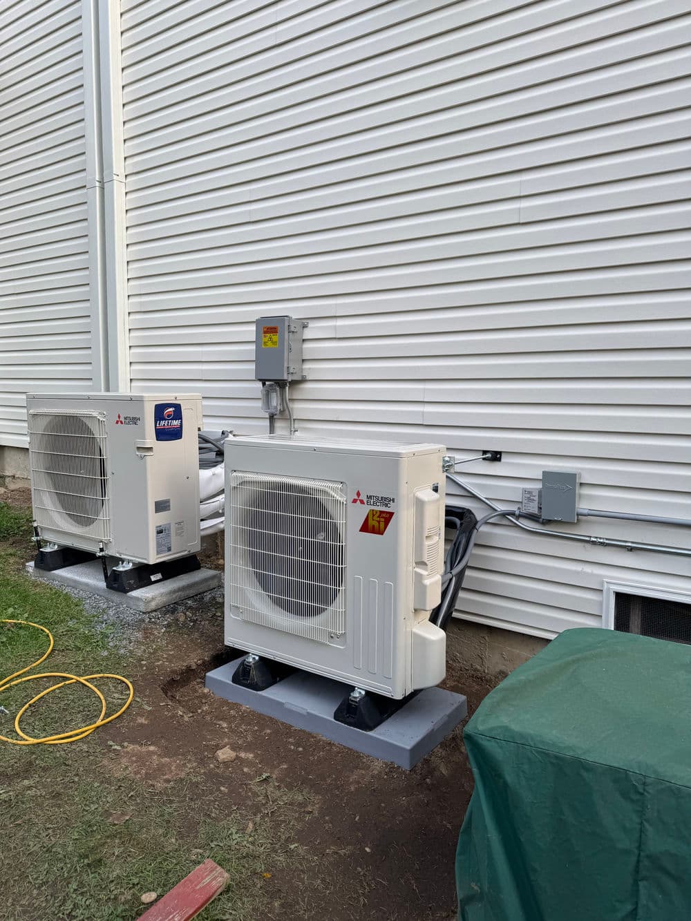Mitsubishi air conditioning units installed outside a building against a textured wall.