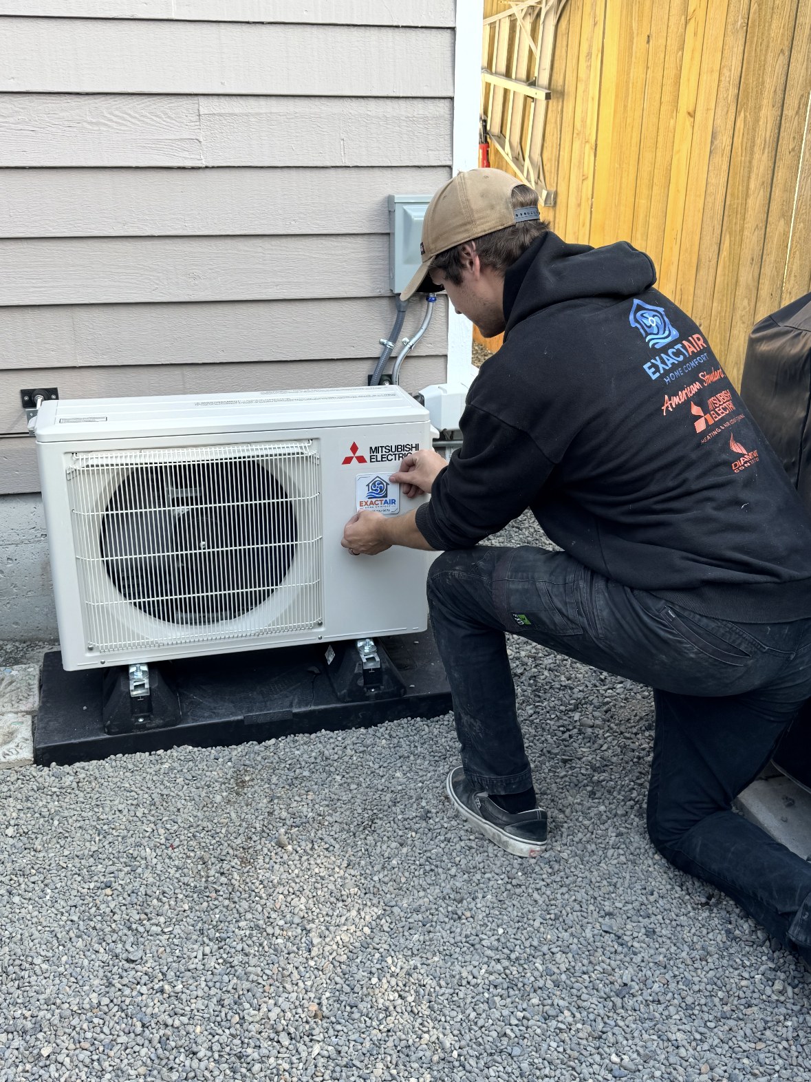 Rylan Utter of ExactAir Home Comfort badging a newly installed Mitsubishi Electric heat pump outdoor unit near Everett, WA