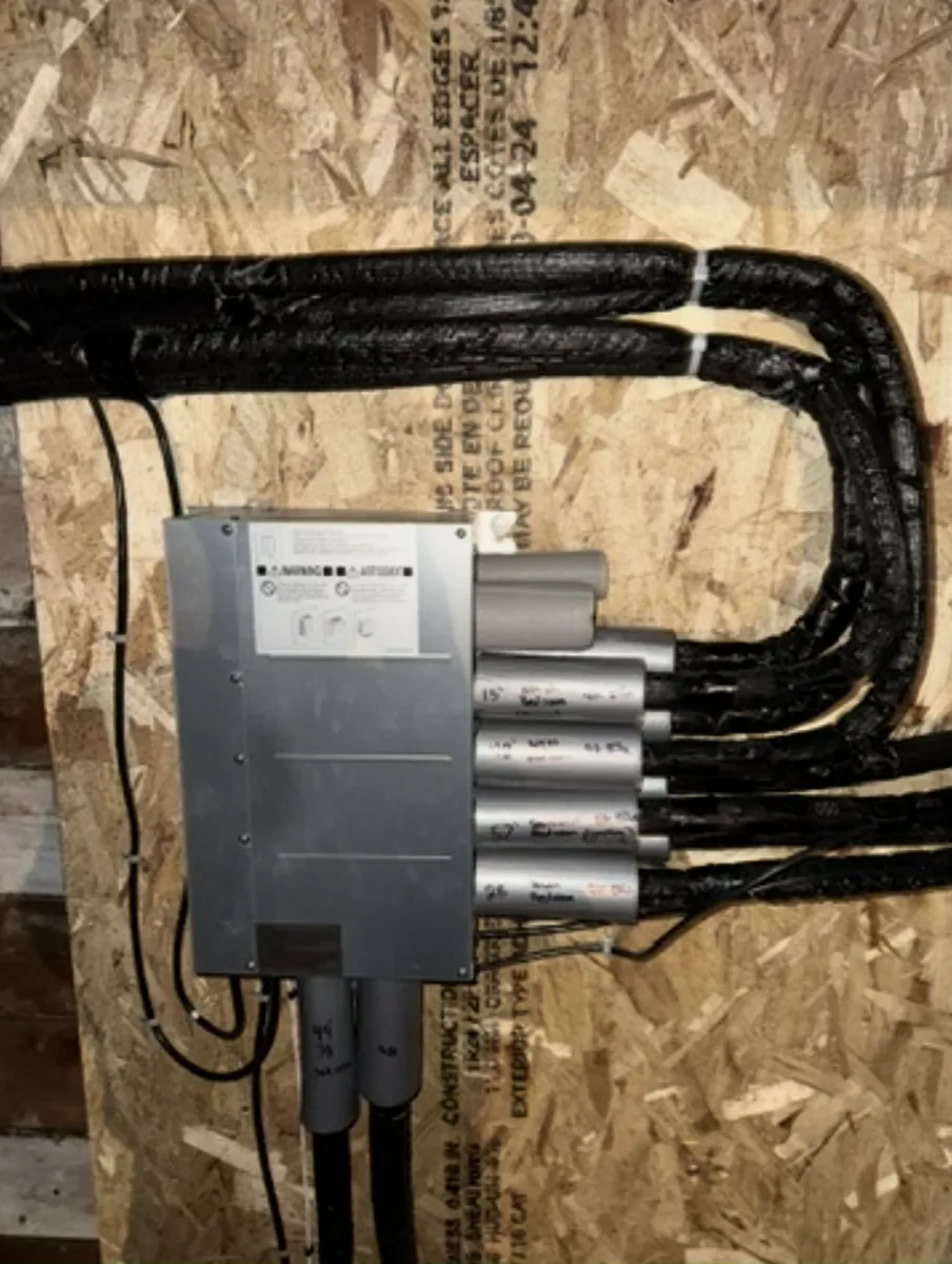 Branch box for a multi-zone ductless heat pump system, each line set labelled by hand with the room it serves and its run length.